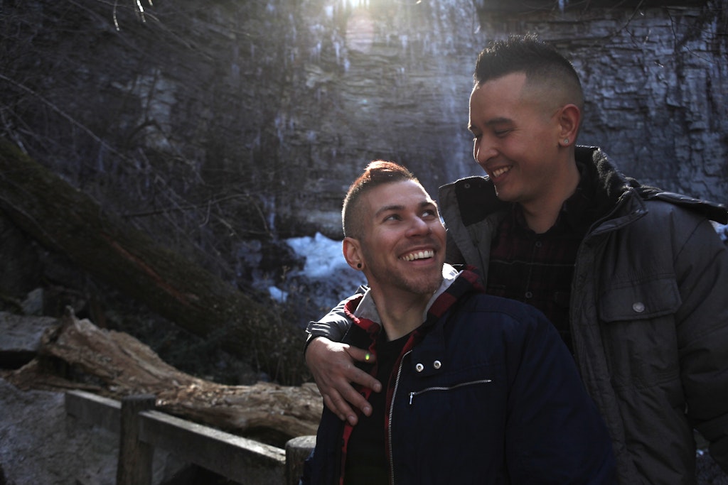 Two men snuggle as they look over a frozen waterfall. 